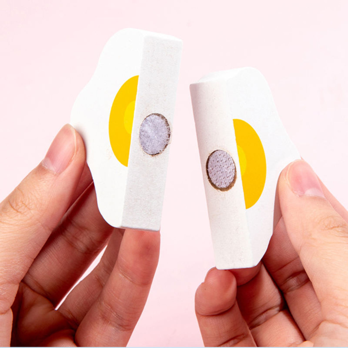 Two small round earrings with yellow and gray designs held between fingers against a light pink background